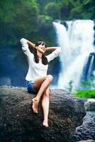 a woman sitting on a rock near a waterfall photo