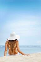 un mujer en un blanco sombrero sentado en el playa foto