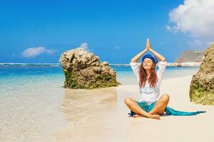 un mujer es sentado en el playa haciendo yoga foto