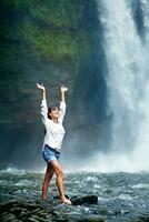 a woman standing in front of a waterfall with her arms up photo