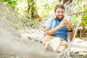 a man is sitting in a hammock and using his phone photo