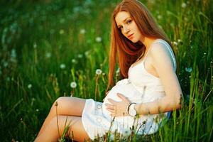 a pregnant woman sitting in a field with dandelions photo