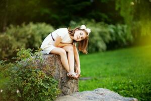 a young girl sitting on a rock in a field photo