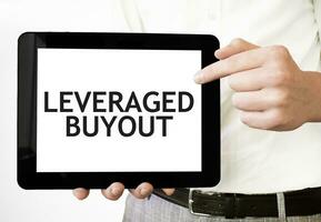 Text LEVERAGED BUYOUT on tablet display in businessman hands on the white background. Business concept photo