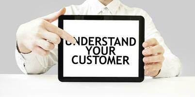 Text UNDERSTAND YOUR CUSTOMER on tablet display in businessman hands on the white background. Business concept photo