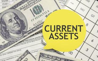 CURRENT ASSETS words on yellow sticker with dollars and charts photo