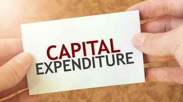 CAPITAL EXPENDITURE word inscription on white card paper sheet in hands of a businessman. recap concept. red and white paper photo