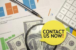 CONTACT US NOW words on yellow sticker with dollars with calculator and pen photo