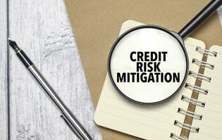 CREDIT RISK MITIGATION words on magnifier glass with notebook and pen photo