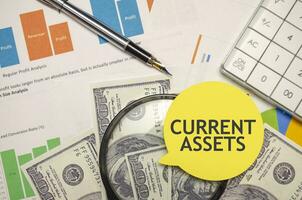 CURRENT ASSETS words on yellow sticker with dollars with calculator and pen photo