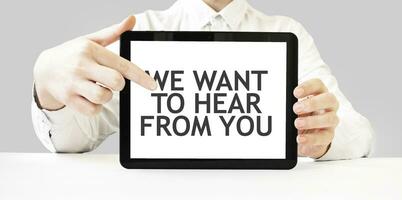 Text WE WANT TO HEAR FROM YOU on tablet display in businessman hands on the white background. Business concept photo