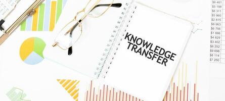 Text KNOWLEDGE TRANSFER. on white notepad, glasses, graphs and diagrams. photo