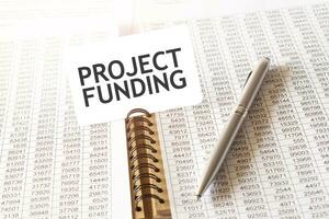 Text PROJECT FUNDING on paper card,pen, financial documentation on table photo