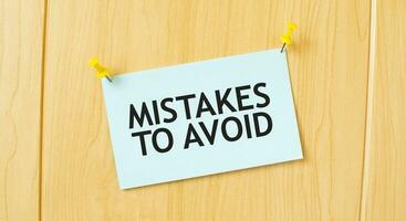 MISTAKES TO AVOID sign written on sticky note pinned on wooden wall photo