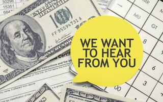 WE WANT TO HEAR FROM YOU words on yellow sticker with dollars and charts photo