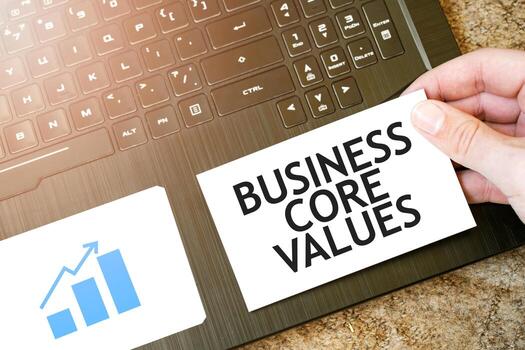 Calculator, red notepad, three colour pencils, silver pen and brown notebook with text BUSINESS CORE VALUES, photo