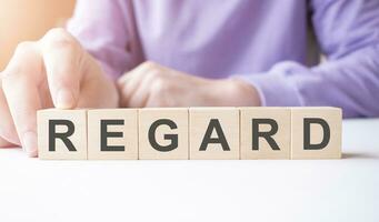 Businessman hand holding wooden cube block with REGARD business word on table background. photo