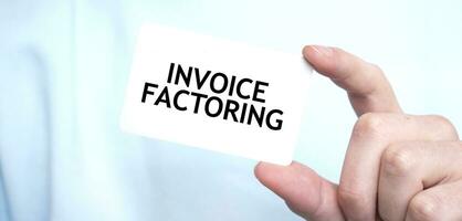 Man in blue sweatshirt holding a card with text INVOICE FACTORING, business concept photo