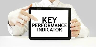 Text KEY PERFORMANCE INDICATOR on tablet display in businessman hands on the white background. Business concept photo