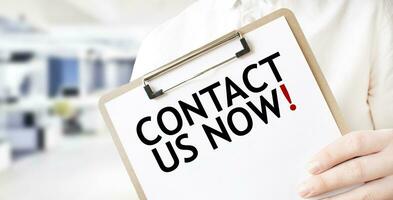 Text CONTACT US NOW on white paper plate in businessman hands in office. Business concept photo