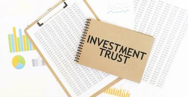 Text INVESTMENT TRUST on brown paper notepad on the table with diagram. Business concept photo