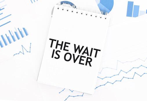 White notepad with text THE WAIT IS OVER on the financial documentation. Finance and business concept photo