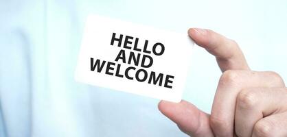 Man in blue sweatshirt holding a card with text HELLO AND WELCOME, business concept photo