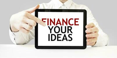 Text FINANCE YOUR IDEAS on tablet display in businessman hands on the white background. Business concept photo