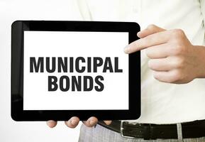 Text MUNICIPAL BONDS on tablet display in businessman hands on the white background. Business concept photo