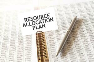 Text RESOURCE ALLOCATION PLAN on paper card, pen, financial documentation on table photo