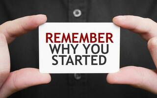 Businessman holding a card with text REMEMBER WHY YOUR STARTED, business concept photo