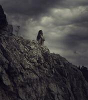 un mujer sentado en parte superior de un montaña con oscuro nubes foto