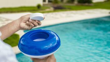 Hands holding a dispenser with pool chlorine tablet, pool float and chlorine tablets for pool maintenance. Hands holding a pool chlorine dispenser photo