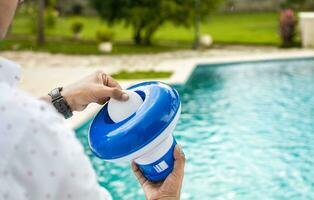 Pool float and chlorine tablets for pool maintenance. Hands holding a pool chlorine dispenser. Hand of a pool disinfection worker holding a dispenser with a chlorine tablet photo