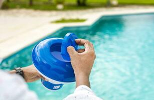 manos de un trabajador instalando un piscina cloro flotar, un persona participación un piscina cloro dispensador. manos participación un piscina cloro dispensador foto