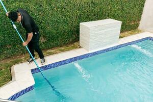 Maintenance person cleaning a swimming pool with skimmer, Worker cleaning a pool with skimmer. Swimming pool cleaning and maintenance concept photo