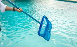 un hombre limpieza piscina con hoja desnatadora. hombre limpieza el piscina con el desnatadora, persona con desnatadora limpieza piscina, manos participación un desnatadora con azul piscina en el antecedentes foto