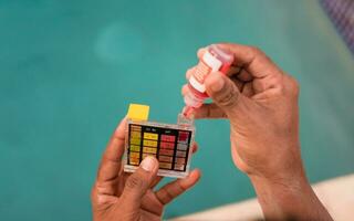 Testing the chlorine and PH of swimming pool. Close up of person testing the ph of the water with mini tester in swimming pool. Hand testing pool water for chlorine with PH mini tester photo