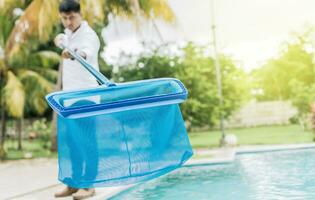 Person with skimmer cleaning pool. Man cleaning the pool with the Skimmer, A man cleaning pool with leaf skimmer. Hands holding a skimmer with blue pool in the background photo