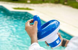 Hands of a worker installing a pool chlorine float, a person holding a pool chlorine dispenser. Hands holding a pool chlorine dispenser photo