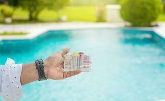Hand holding Water Test Kit on blurred pool background, Hand holding a pool ph and chlorine tester, Person holding complete water test kit with blurred pool background photo