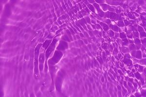 Purple water with ripples on the surface. Defocus blurred transparent pink colored clear calm water surface texture with splashes and bubbles. Water waves with shining pattern texture background. photo