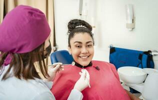 profesional dentista examinando hembra paciente en oficina. cerca arriba de sonriente paciente a del dentista oficina mirando a cámara, sonriente paciente en del dentista silla foto