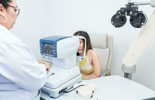 Specialist performing eye exam to female patient. Optometrist checking the eyesight of a patient with an autorefractor photo