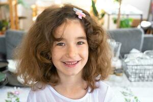 retrato de un contento bebé niña con un alegre y dañoso sonrisa de cerca con corto Rizado cabello. foto