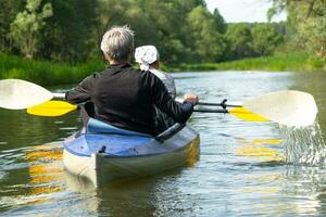 Family kayak trip for seigneur and senora. An elderly married couple rowing a boat on the river, a water hike, a summer adventure. Age-related sports, mental youth and health, tourism, active old age photo