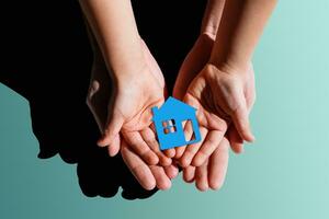 people, charity, family and home concept - close up of woman and girl holding paper house cutout in cupped hands photo