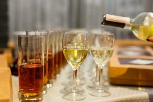 White wine being poured into wine glass in restaurant. Set of glasses with juice photo