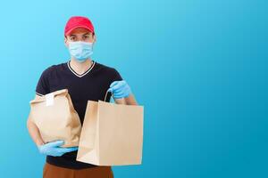 Delivery man in mask and gloves bring fresh food to customer's home. Stay home. Online shopping concept. blue background photo