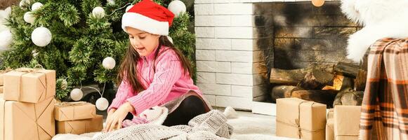 Happy little girl with Christmas present laying by the fire in front of xmas tree photo